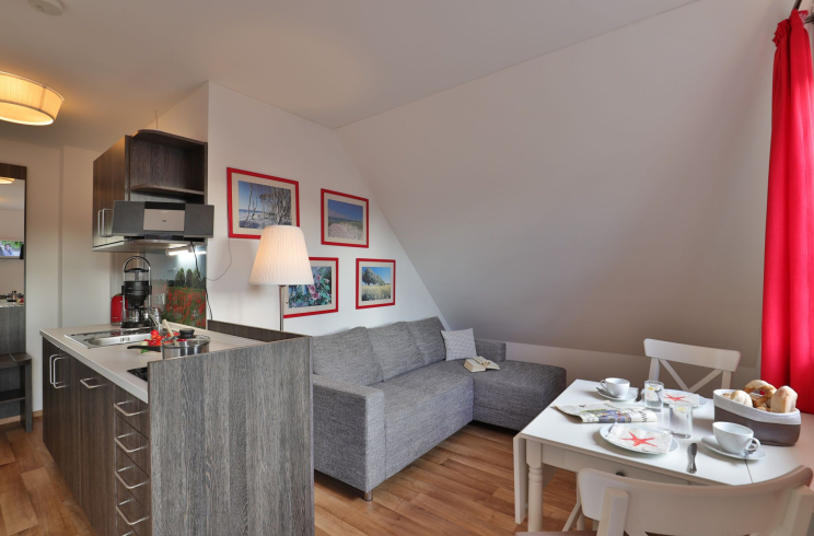 Küchenzeile, graues Ecksofa, Esstisch mit 2 weißen Stühlen