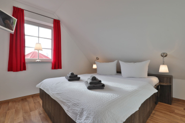 Schlafzimmer mit Doppelbett, TV, Fenster mit roten Gardinen