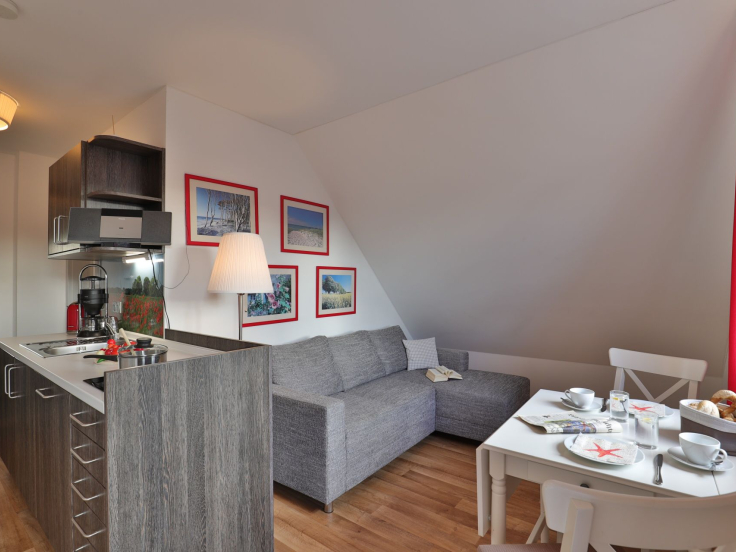 Küchenzeile, graues Ecksofa, Esstisch mit 2 weißen Stühlen