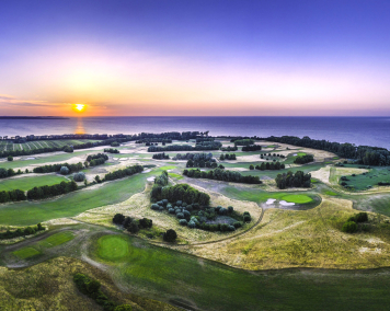 Ein Golfplatz aus der Luft. Im Hintergrund die Ostsee bei Sonnenuntergang.