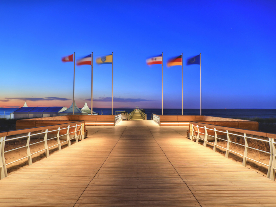 Die Seebrücke Boltenhagen ragt in die Ostsee. Beleuchtet bei Nacht. Fahnen wehen am Ende.
