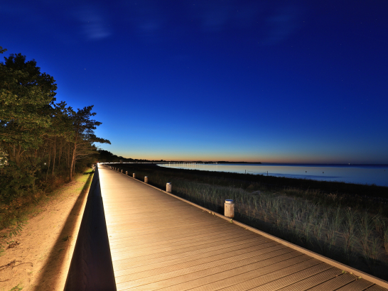 Ein bei Nacht beleuchteter Holzweg entlang des Strandes.