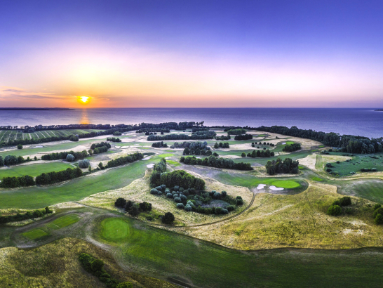 Ein Golfplatz aus der Luft. Im Hintergrund die Ostsee bei Sonnenuntergang.