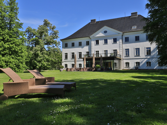 Schloss Schwansee in einem sommerlichen Park. Im Vordergrund stehe Liegestühle.