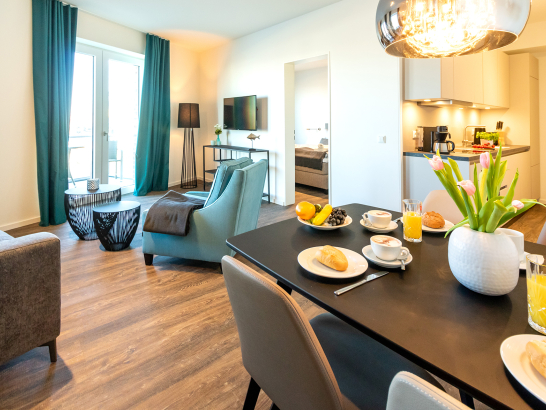 Wohnbereich einer Ferienwohnung mit gedecktem Esstisch und Blick auf die Küchenzeile und in ein der Schlafzimmer
