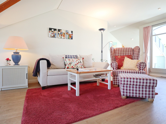 Geräumiger Wohnbereich mit Sitzgarnitur, Teppich und Beisteltisch im Landhausstil und weiß-roter Farbgebung