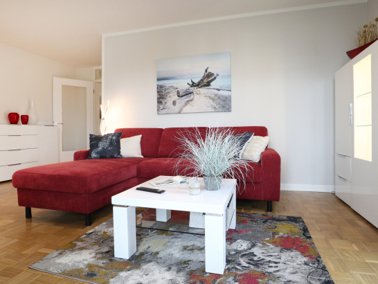 heller Wohnbereich mit rotem Sofa und weissem Beisteltisch