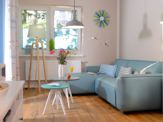 Lichtdurchflutetes Wohnraum mit blauen Sofa und zwei kleinen Couchtischen