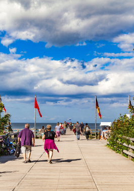 Menschen laufen auf einem Weg. Im Hintergrund die Seebrücke und die Ostsee.